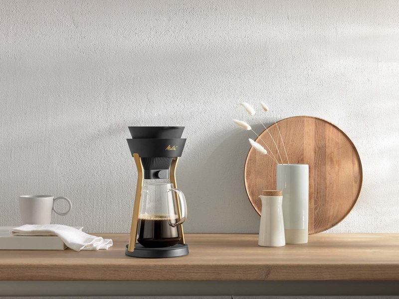 Melitta® EPOS® in an elegant design in black and gold, with the matching Melitta® BLOOM® coffee and Melitta® Pour Over 1X4® filter