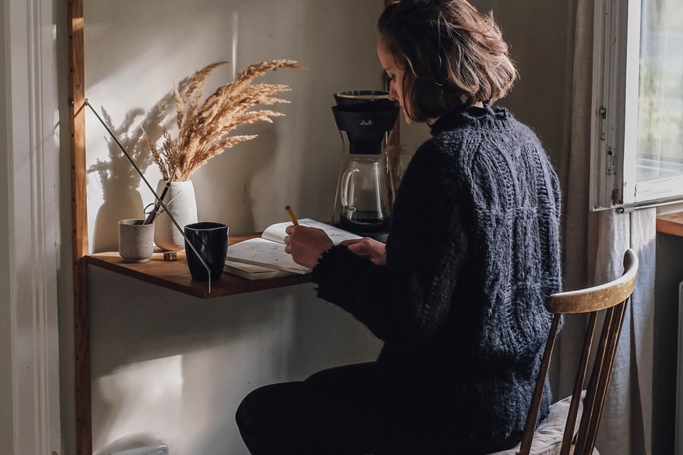 Junge Frau sitzt an Schreibtisch mit Notizbuch und Kaffee.