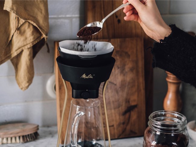 Gemahlener Kaffee wird mit einem Löffel in einen manuellen Kaffeezubereiter gestreut.