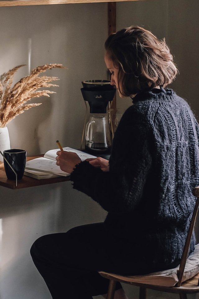 Junge Frau sitzt an Schreibtisch mit Notizbuch und Kaffee.