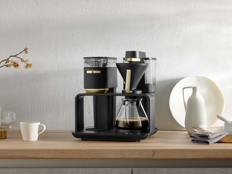 Melitta® EPOS® in an elegant design in black and gold, with the matching Melitta® BLOOM® coffee and Melitta® Pour Over 1X4® filter